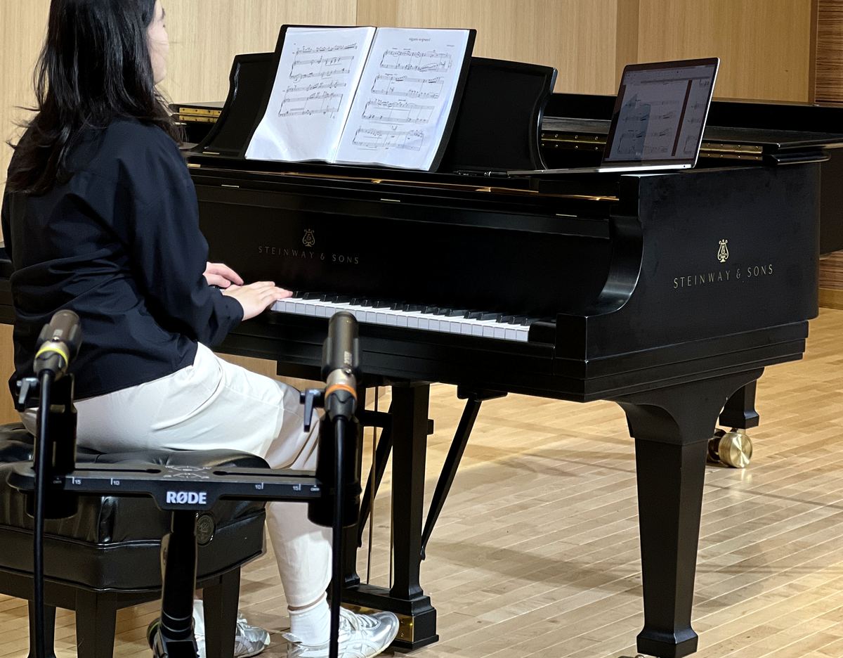 教師於音樂廳以 Steinway & Sons 三角鋼琴排練，譜架上為樂譜與電子譜面